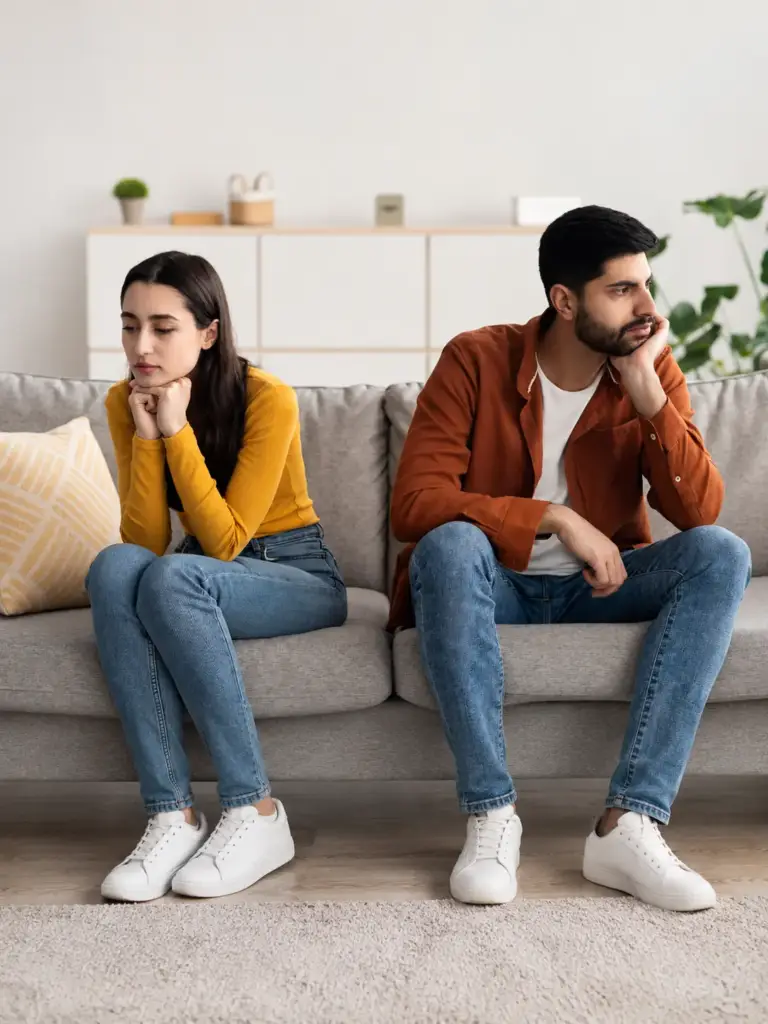 Husband and wife sitting on a sofa looking distant, husband wife problem solution by astrologer Devraj Sharma